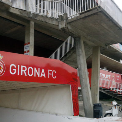 En primer terme, el cartell amb el rètol del Girona FC; al fons, l'estadi de Montilivi