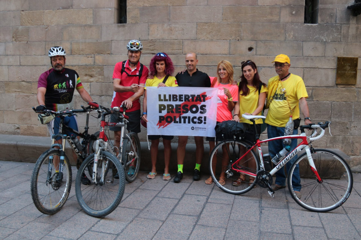 Els tres ciclistes, amb altres persones que els acompanyaven, mostrant una pancarta reclamant l'alliberament dels presos, abans d'iniciar la pedalada a la plaça Paeria de Lleida
