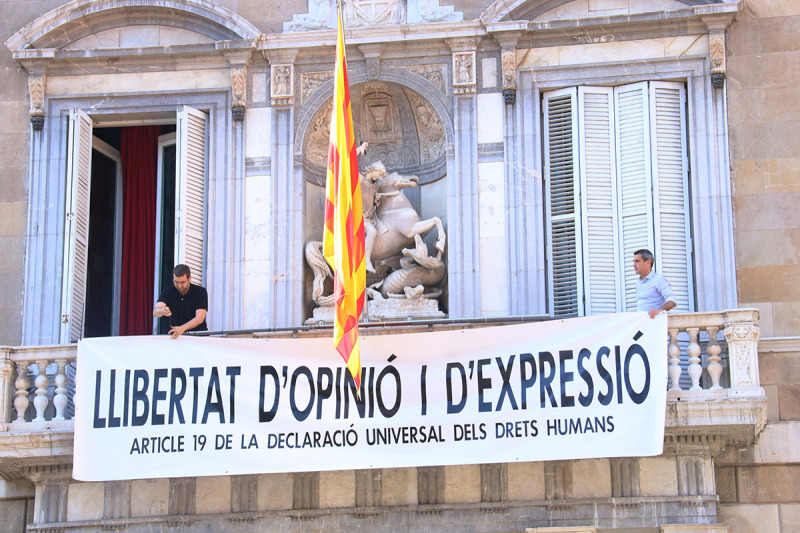 Membres de l'equip del president del Govern, Quim Torra, pengen la nova pancarta a la façana de Palau: "Llibertat d'opinió i d'expressió. Article 19 de la Declaració Universal dels Drets Humans", a plaça Sant Jaume, el 22 de març de 2019