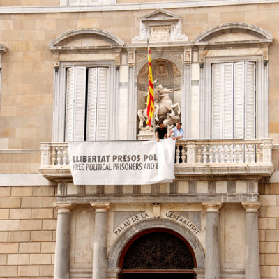 Pla general de la façana de la Generalitat on es veu la pancarta en favor de la llibertat dels presos mig plegada en el moment de treure-la